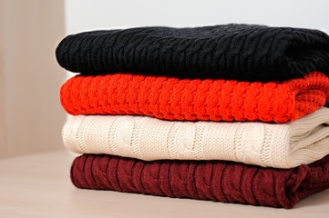 Different knitted sweaters  in a wardrobe, close up. Concept warm clothing.