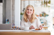 Cheerful young woman is having breakfast in cafe and smiling positively at the camera. The concept of breakfast and good mood in the morning.