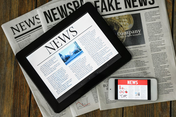 Newspapers, tablet computer and phone with news on screen on wooden table