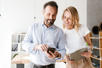 Couple of smiling colleagues looking at mobile phone