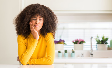 Poster - African american woman wearing yellow sweater at kitchen touching mouth with hand with painful expression because of toothache or dental illness on teeth. Dentist concept.