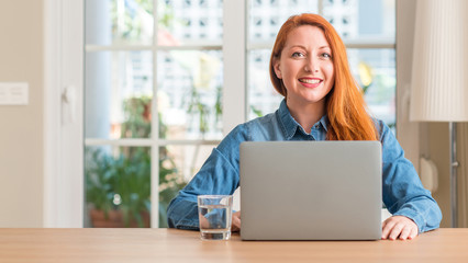 Poster - Redhead woman using computer laptop at home with a happy face standing and smiling with a confident smile showing teeth