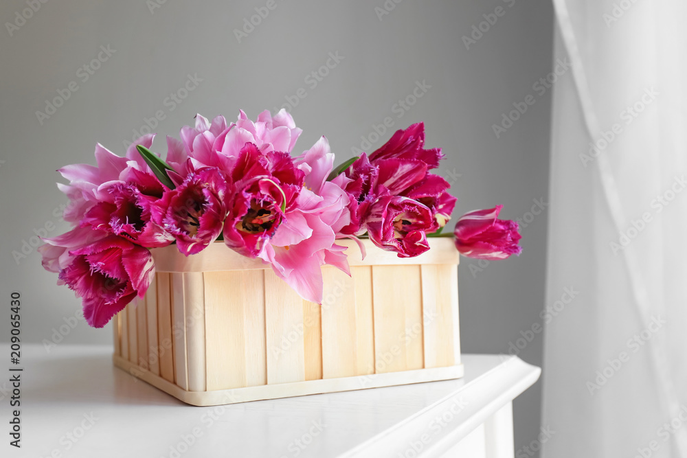 Box with beautiful tulips on table against grey wall