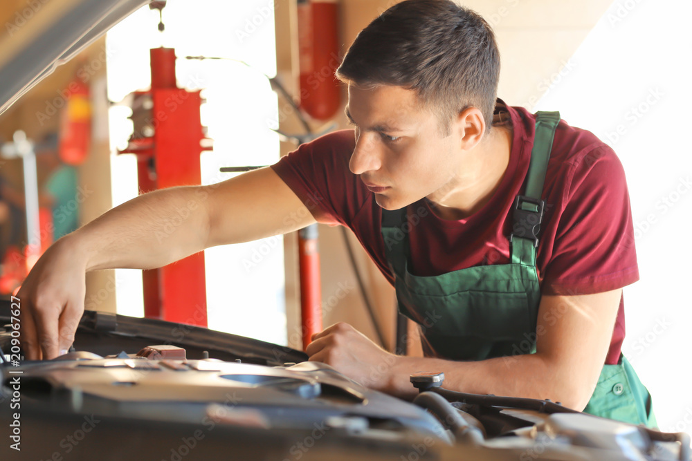 Young auto mechanic repairing car in service center