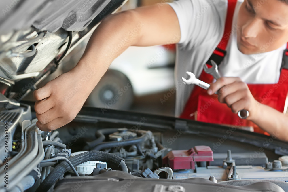 Young auto mechanic repairing car in service center