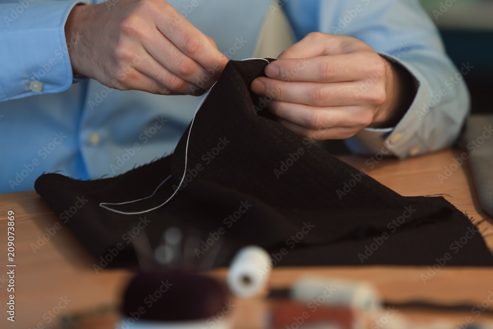 Young tailor sewing at table in atelier, closeup