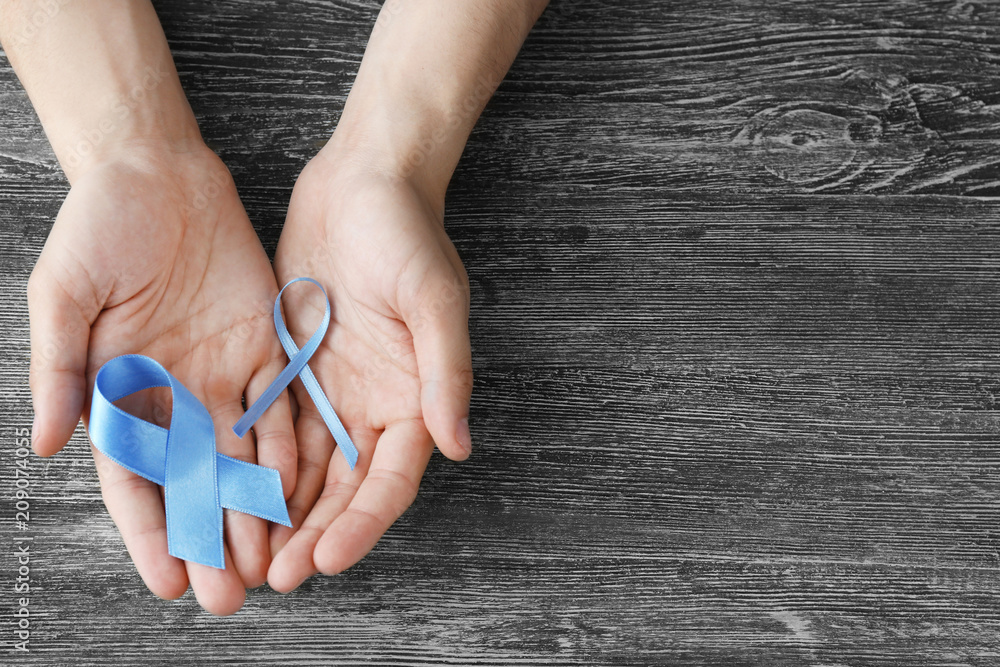 Male hands holding blue ribbons on wooden background. Prostate cancer concept