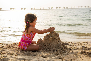 Cute little girl playing with sand and building sandcastle on the beach in Dubai