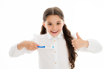 Wall Mural - Girl cute long curly hair holds toothbrush white background. Child girl holds toothbrush with paste and shows thumbs up. Child school girl smart kid happy face cares hygiene. Brush teeth concept