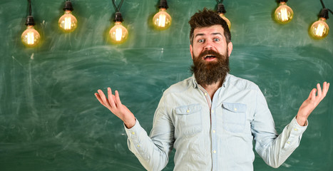 Man with beard and mustache on confused face stand in front of chalkboard. Difficulties concept. Bearded hipster in shirt, chalkboard on background. Guy bewildered with confusing expression.