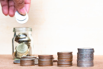 Wall Mural - Saving money concept. Close up finger hold stack coins into bottle arrangement with shown concept of growing business and wealthy.