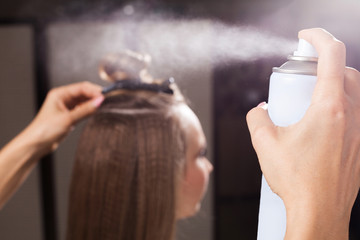 Wall Mural - hairdresser fixing a coiffure with a topknot of a young beautiful woman using a hair spray in a beauty salon. concept of professional stylist studying