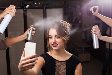 beautiful happy model with perfect makeup and coiffure is having fixation with hair sprays. four hands holding and pulverizing bottles. girl is taking a photo of herself