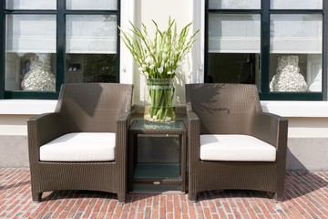 Two chairs and table with flowers in front of white house  