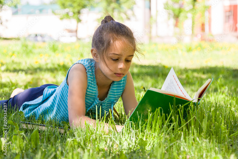 Cute serious little girl lying on a green grass in summer city park and ...