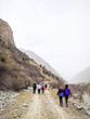 © Konstantin Savusia - Group of hikers walking in mountains. A group of people with backpacks walking along the road. There are mountains from left. The sky is cloudy.