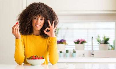 Poster - African american woman eating strawberries at home doing ok sign with fingers, excellent symbol