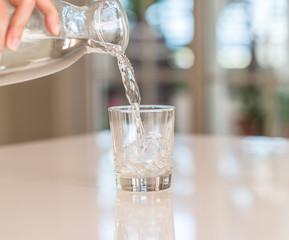 Wall Mural - Closeup of bottle pouring watter in a glass on the table with sunny bokeh background at home.