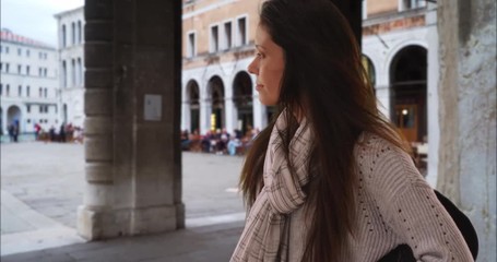 Wall Mural - Millennial woman with backpack in Venice people-watching near Grand Canal, Female traveler backpacking in Italy stands on city street looking away from camera, 4k