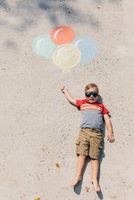 Cute Young Boy With Sunglasses Holding On To Balloons Drawn On The Ground