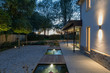 © phillipsvisuals/Stocksy - Exterior of a modern house and garden illuminated at night.