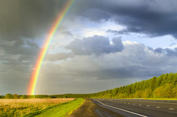 wet highway after rain with a rainbow against the backdrop of a rainy sky