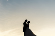 Silhouette Of Bride And Groom Embracing Each Other At Sunset