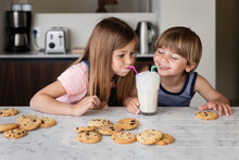 Boy And Girl Blowing Bubbles In Glass Of Milk With Straws