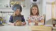 © KONSTANTIN SHISHKIN - Two little sisters smiling with homemade cookies and cups of tea at cooking studio