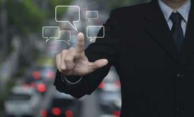 Businessman point to social chat sign and speech bubbles over blur of rush hour with cars and road, Social network concept