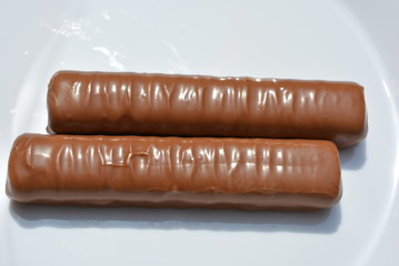 On a white plate of glass are two chocolate bars with a sandy liver and caramel, covered with a layer of milk chocolate