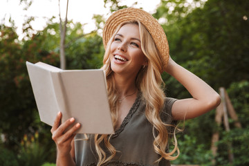 Wall Mural - Happy woman in straw hat holding book and looking away