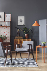 Wall Mural - Living room interior with armchairs, orange lamp and coffee table, and wooden cabinets in the background on the grey wall