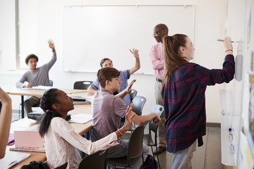 Female High School Pupil Writing On Whiteboard In Class