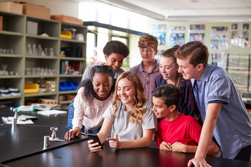 Wall Mural - Group Of High School Students Looking At Message On Mobile Phone In Classroom