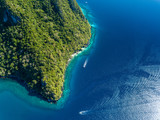 Fototapeta Natura - Aerial drone view down onto boats over a tropical coral reef surrounded by mountains and jungle