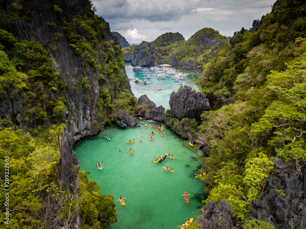 Aerial drone view of a beautiful tropical lagoon filled with kayaks and surrounded by jagged limestone cliffs (Small Lagoon, Miniloc Island, El Nido) - obrazy, fototapety, plakaty 