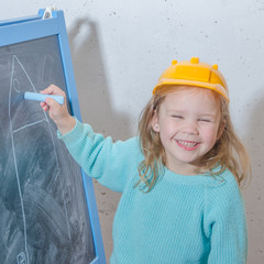 girl in a helmet paint a house on a chalk Board