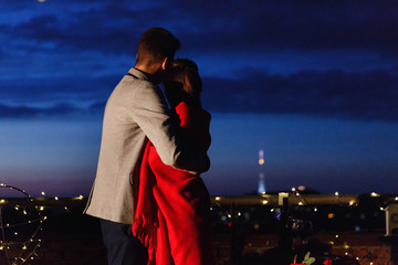 Boy and girl hug each other tender standing on the rooftop in the rays of evening lights and having a romantic dinner