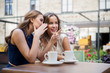 communication and friendship concept - smiling young women drinking coffee and gossiping at street cafe