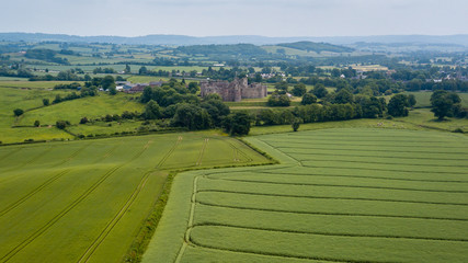 Canvas Print - Aerial drone view of an ancient castle behind cultivated farmland and fields