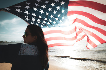 USA Independence day, 4 July. Close up oung happy woman holding United States of America flag and running, jumping carefree with open arms on the beach.