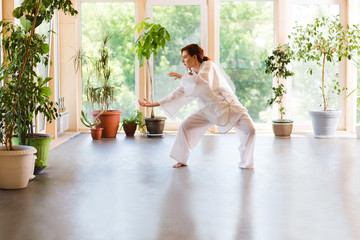 Wall Mural - Young Woman praticing tai chi chuan in the gym. Chinese management skill Qi's energy.