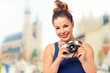 © WDnet Studio - Vacation photographer concept - beautiful and attractive woman holding a retro SLR camera and smiling on blurred background of a historic city (vintage effect).