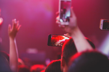 A crowded concert hall with scene stage lights, rock show performance, with people silhouette and hand holding smartphone