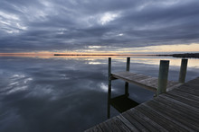 Dock On Ocean Inlet With Dramatic Clouds Reflecting In Water