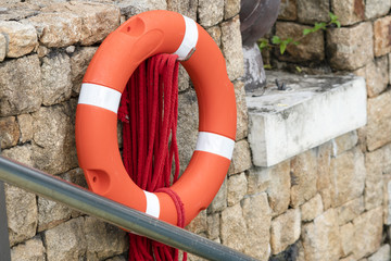 Red Life buoy hanging on stone wall for helping people in a water accident.Safety equipment beside the pool