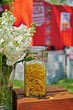 A glass jar filled with dry yellow Fusili Italian pasta on a wooden box with a bunch of white stock flowers in a vase and outdoor background. Selective focus.
