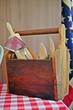 Variation of rural and vintage cooking and kitchen utensils in a wooden storage box on a table with American flag background.