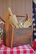 Variation of rural and vintage cooking and kitchen utensils in a wooden storage box on a table with American flag background.